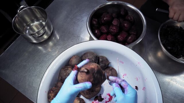 A cook in the kitchen exemine cooked beets, then peels with a knife