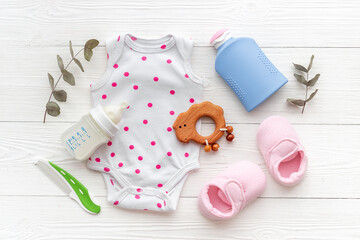 Set of baby hygiene cosmetic products - shampoo and soap with a comb. Eco friendly accessories - bodysuit and wooden toys with bottle of milk on white wooden background, top view