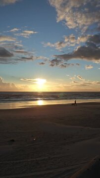Serene sunset at Cuesta Maneli Beach with a person walking a dog along the shoreline, warm golden light, dramatic clouds, and peaceful Atlantic coastal scenery.