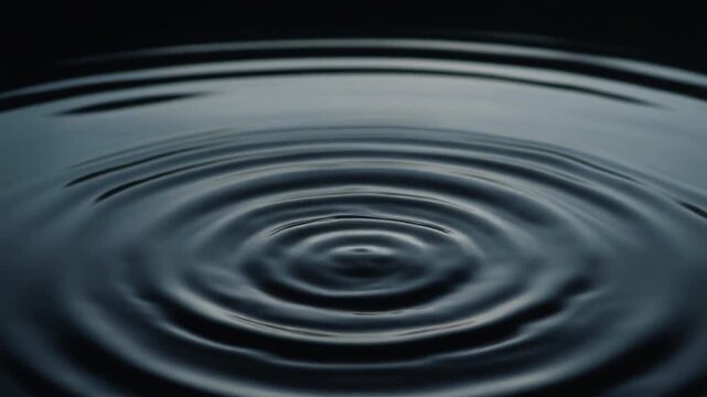 Ripples spreading across perfectly still black water as a single droplet falls