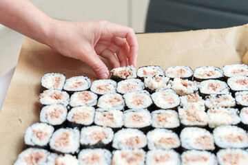 Arranging delectable tuna maki sushi rolls on parchment paper, a culinary artist finalizes preparation in a bright kitchen © andov