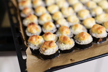 Rows of freshly baked sushi rolls with rice, seaweed, and baked creamy topping on parchment paper on a metal baking sheet