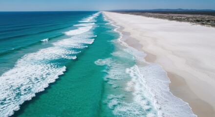Wide, turquoise ocean waves meet a pristine white sand beach.  Aerial view