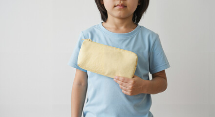 Young child holding a yellow pencil case while wearing a blue shirt  