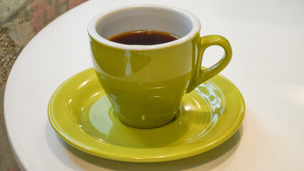 a glass of hot americano in a green glass cup placed on the edge of a wooden table