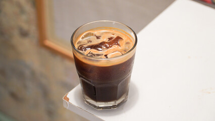a glass of iced americano in a clear glass placed on the edge of a wooden table