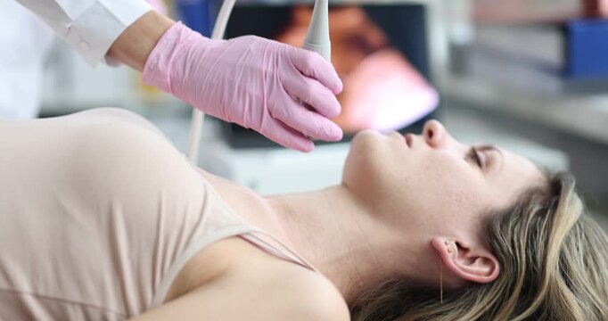 Female doctor hand with pink glove presses ultrasound probe on neck. Patient woman lies on couch receiving thyroid ultrasound scanning examination