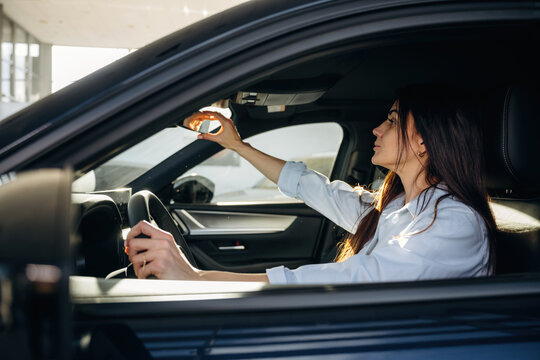 Adjusting the mirror. Woman is sitting in the modern car, happy new owner - Powered by Adobe