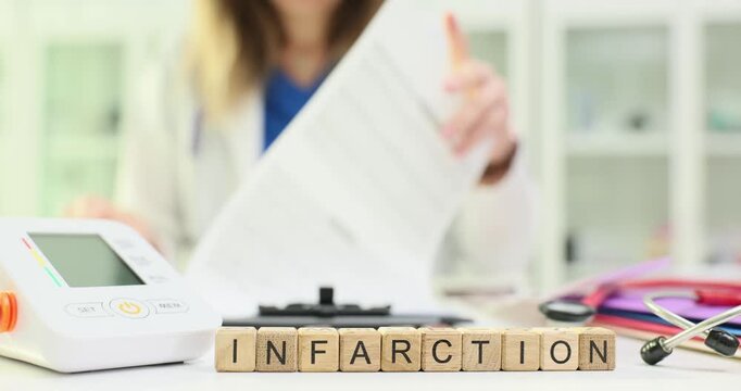 Wooden blocks spell word Infarction near digital heart monitor. Cardiology doctor checks patient records assessing infarction risk after attack