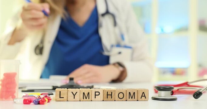 Wooden blocks spell word Lymphoma near scattered pills on desk. Oncology doctor writes case notes discussing lymphoma stage and therapy at appointment