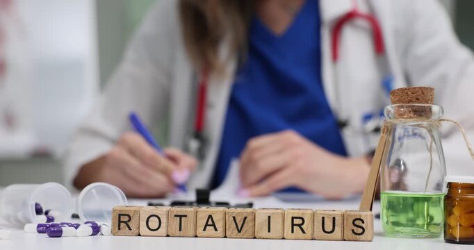 Wooden blocks spell word Rotavirus near green solution in bottle. Infectious disease specialist writes notes studying rotavirus spread at appointment