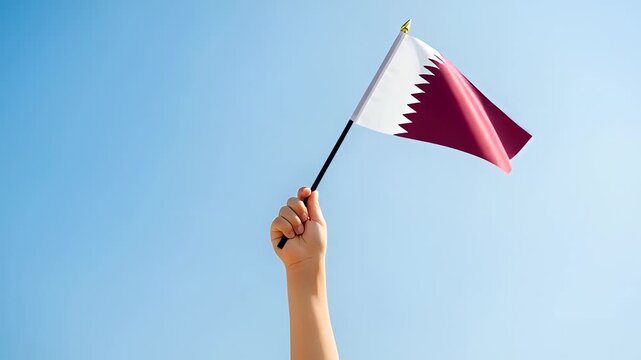 Hand holding Qatar flag against a clear blue sky background, celebration