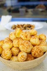 Vertical close-up of a woven straw basket filled with freshly baked Pão de Queijo (Brazilian Cheese Bread), featuring its characteristic golden, spotted crust. Pão de Queijo is a popular Brazilian del