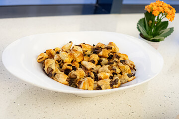 Oval white platter filled with mini chocolate puff pastry croissants or rolls, set on a light-colored countertop. The image, captured indoors with natural light, suggests a coffee break, afternoon sna