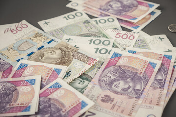 Various denominations of Polish zloty banknotes scattered on a table with shallow depth of field, symbolising cash savings spending inflation finance and economic concepts