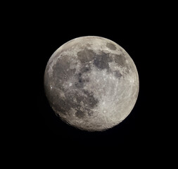 Close-up of a bright full moon in the night sky. Visible surface details, craters, and dark areas create a contrasting pattern. The black background highlights the shape and texture of the lunar disk.