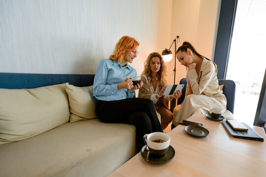 Businesswomen engaging in a collaborative discussion over coffee while reviewing content on a tablet in a modern cafe environment - Powered by Adobe