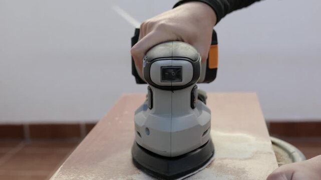 Battery-powered sander smoothing rough spots on wooden surface