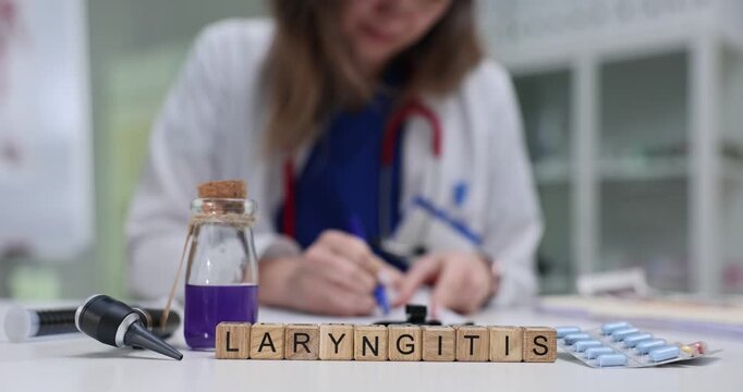 Wooden blocks spell word Laryngitis near purple solution bottle on table. Woman doctor checks throat notes planning therapy for laryngitis treatment