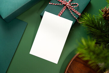 White greeting card with dark green gift box on dark green background decorated with Christmas...