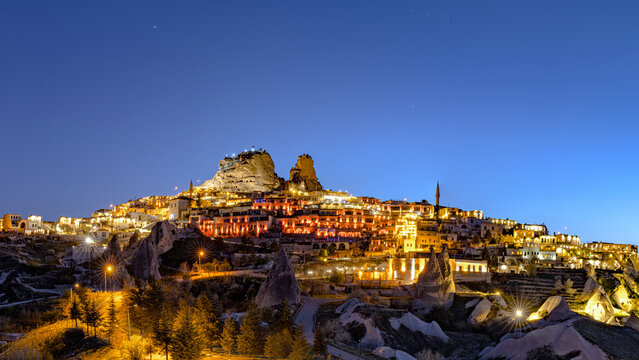 View of dwellings glow warmly on a rocky hillside under a deepening blue sky, a celestial town carved in stone, Uchisar, Cappadocia, Turkey.