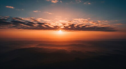 Sunset over misty mountains with orange sky and clouds