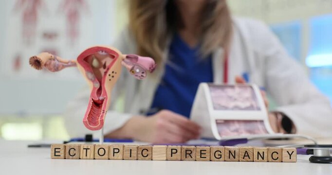 Wooden blocks spell phrase Ectopic Pregnancy near uterus model. Gynecology doctor studies ultrasound scan explaining ectopic pregnancy risk factors
