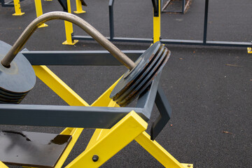 Heavy weight plates rest on a sturdy outdoor gym frame designed for strength training in a public fitness area under bright sunlight