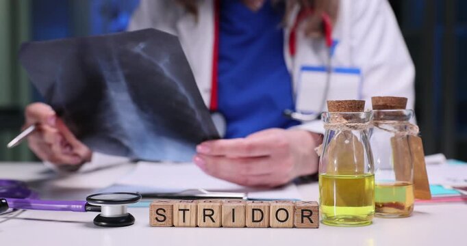 Wooden blocks spell word Stridor near stethoscope and glass bottles on table. Medical worker studies chest x-ray relating stridor sound to image