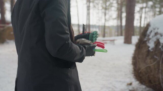 black stablehand preparing grooming brushes outdoors snow-dusted hay bale wooden fence gloved hands holding red and green brushes quiet morning routine tactile focus on tools and motion