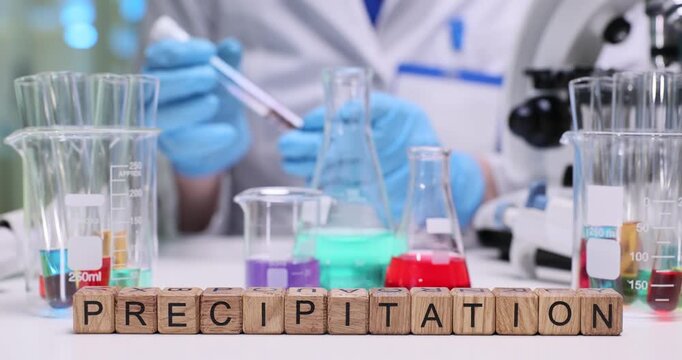 Lab assistant tracks formation of possible particles in liquid inside test tube. Wooden blocks aligned in precise line form term Precipitation