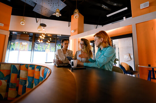 Businesswoman collaborating with colleagues in a modern office cafe during a daytime meeting discussing project ideas - Powered by Adobe