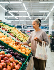 Obraz premium Elderly Woman Choosing Fresh Fruits in Grocery Store Produce Aisle