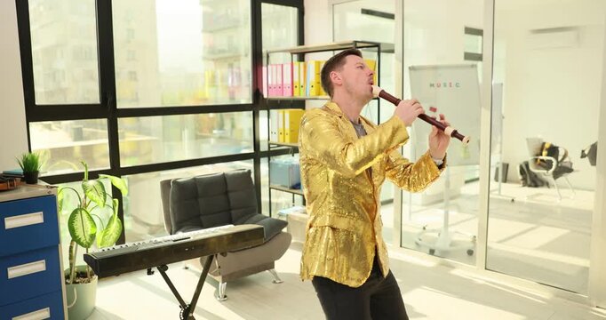 Young man in shimmering golden jacket plays sopilka in office premise. Musician produces traditional Ukrainian melodies on sopilka. Slow motion