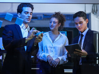 Group of diverse business partnership are brainstorming, writing on a transparent glass whiteboard, and reviewing digital plans. Successful teamwork, innovative corporate strategy, app development