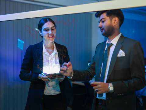 Two diverse business colleagues in collaborative teamwork in the office. Brainstorming and writing ideas on a glass whiteboard. Successful partnership for tech development or corporate strategy plan