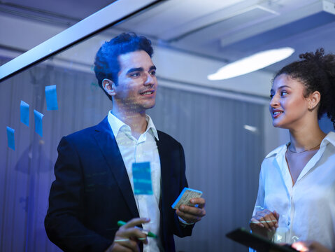 Team of business professionals is focused on strategic development in tech office. Writing on glass board with sticky notes for innovative technology planning and successful project execution.