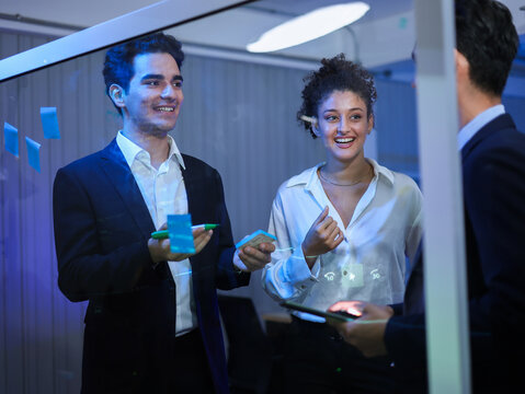 Diverse team of business collaborating and brainstorming project showing idea on glass board with sticky notes and digital tools. Successful innovation, digital transformation, problem-solving - Powered by Adobe