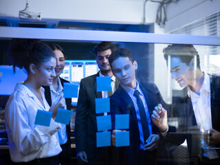 Diverse business group analyzing data and brainstorming ideas using sticky notes on a glass board. Collaborating on developing a strategic solution. Software developer, future tech team at the office