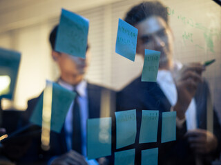 Business team collaborating tech office, strategically utilizing a glass whiteboard and sticky notes to visualize data and brainstorm innovative ideas. Corporate teamwork, planning strategy