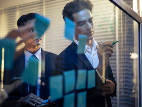 Diverse business team explaining strategic planning in a futuristic. Collaborating on ideas, writing on a transparent board, using digital tablets for successful. Corporate development and innovation - Powered by Adobe