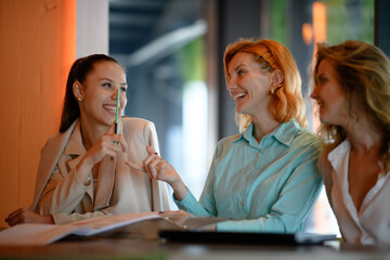Smiling businesswomen collaborating on project at indoor office, having informal discussion about business strategy and team goals, enjoying teamwork