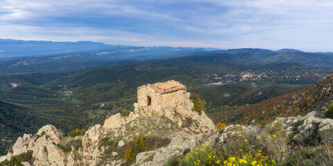 Aerial view of a stone building atop a rocky outcrop overlooking a vast mountainous landscape under blue sky