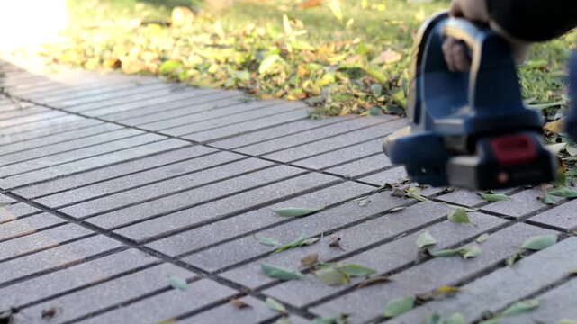 Cordless leaf blower gathering scattered leaves across tile walkway