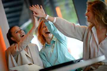 Successful team of businesswomen celebrating a deal with a high five at a modern office, showcasing collaboration and achievements