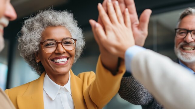 In a bright office space, a group of colleagues shares a moment of joy and camaraderie. Smiles are wide as they exchange high-fives, celebrating their achievements together