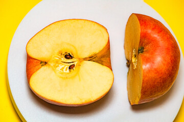 The apple on the white plate is cut in half with a knife