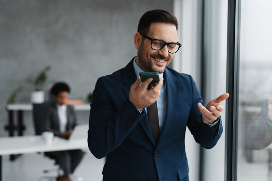 A businessman in a modern office standing near a window and using his smartphone
