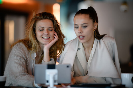 Two women in a business meeting looking at a tablet in a modern cafe during the daytime