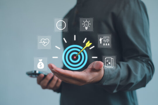 business professional holding a smartphone with digital target and strategy icons, representing goal setting, planning, productivity, performance analytics, and modern business technology. - Powered by Adobe